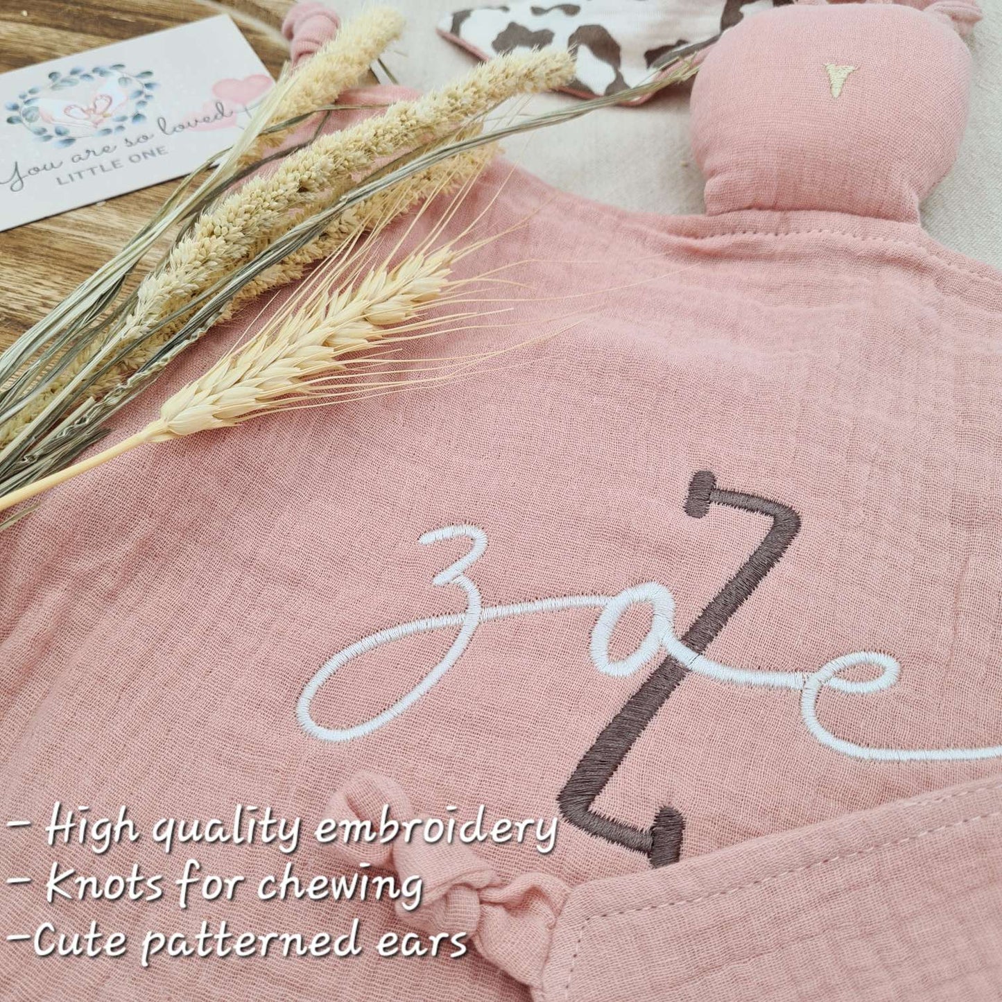 Pink baby comforter with bunny ears, embroidered with name 'Zoe'. Features soft fabric and knots for chewing.