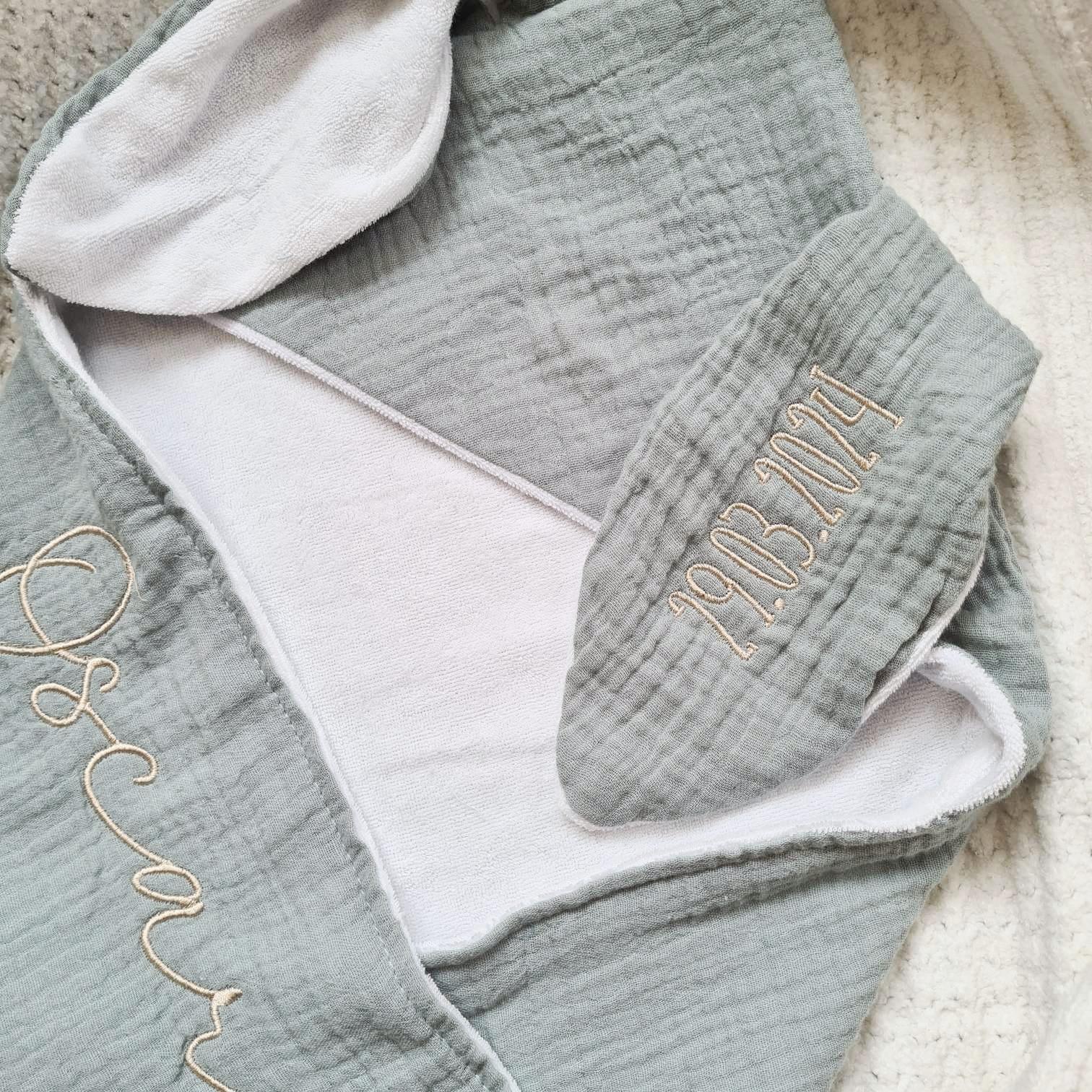 Close-up of green personalised hooded baby towel with embroidered name 'Oscar' and date '19.03.2024'. Soft muslin and terry fabric.