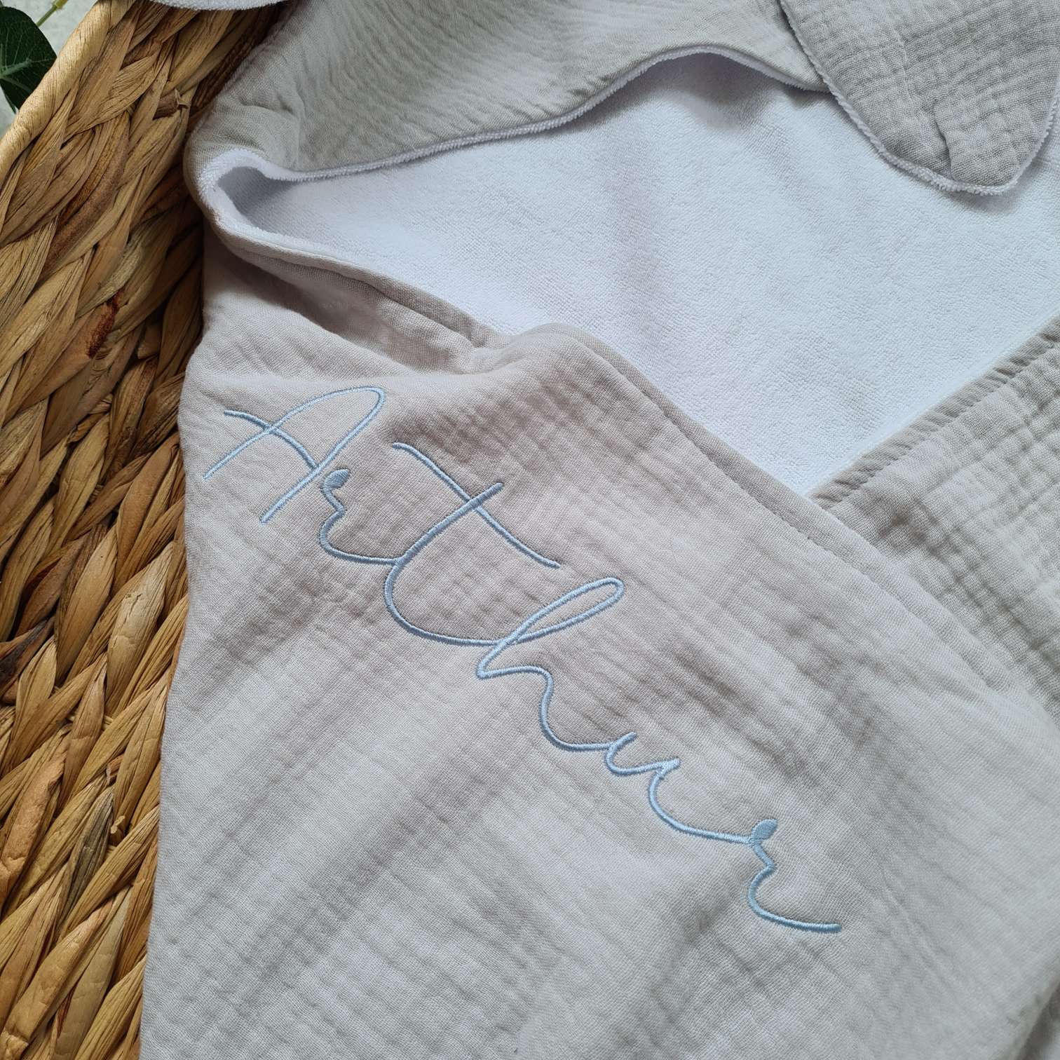 Close-up of grey hooded baby towel with embroidered name 'Arthur'. Soft organic muslin and terry, ideal for newborns.