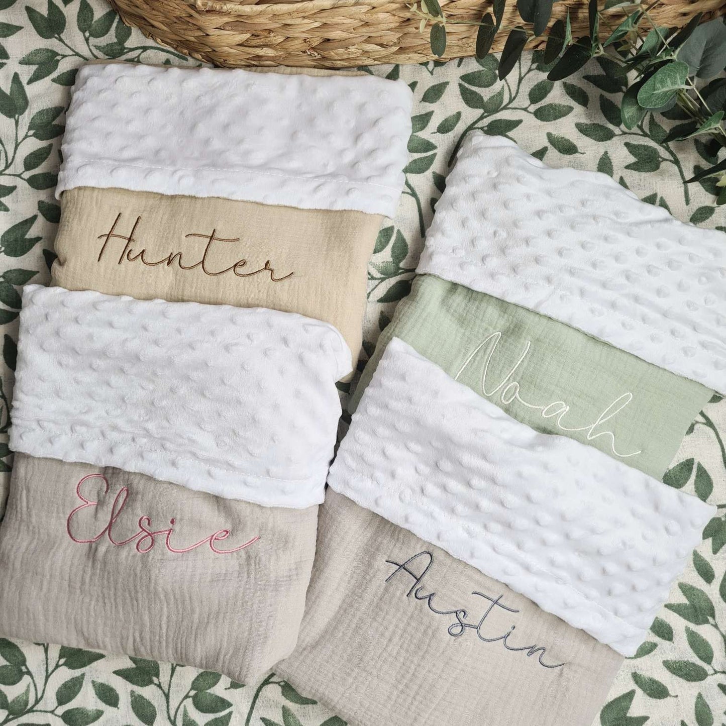 Collection of personalised baby blankets in beige, green, and grey, each embroidered with names'Hunter', 'Noah', 'Elsie', and 'Austin'.