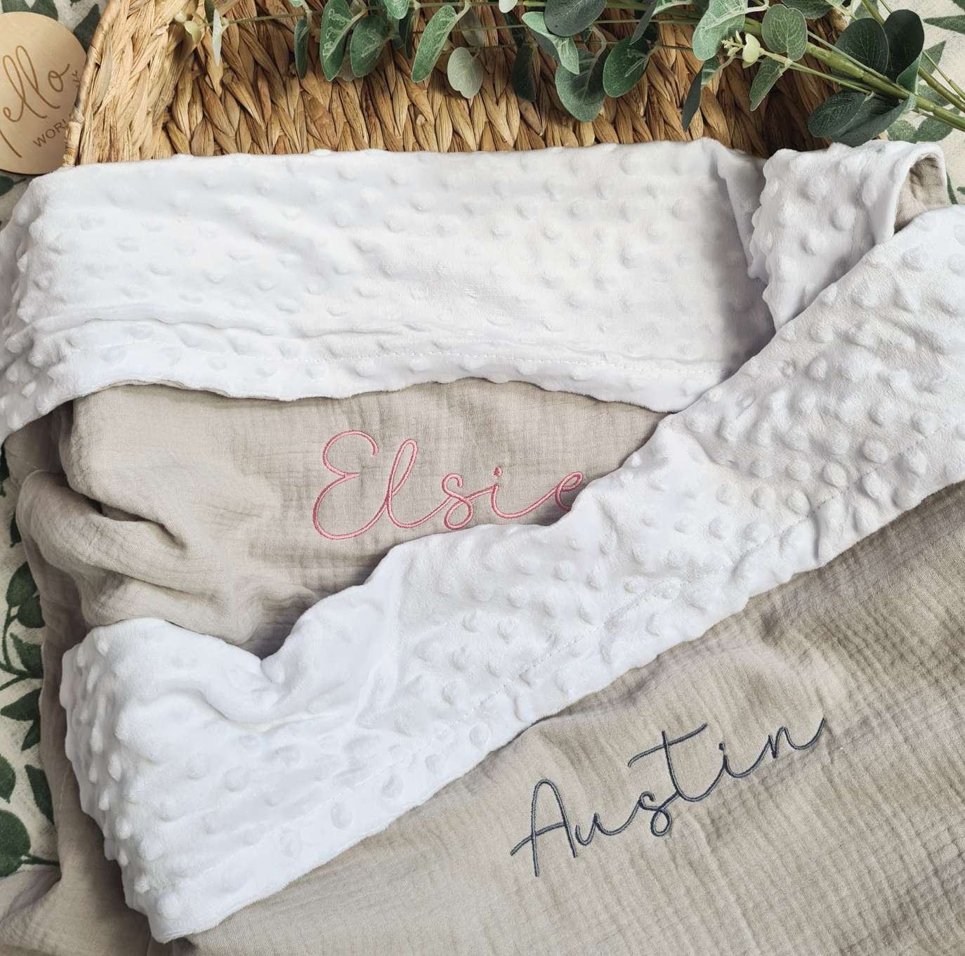 Stacked grey personalised baby blankets with embroidered names 'Elsie' and 'Austin'. Organic muslin with white plush trim.