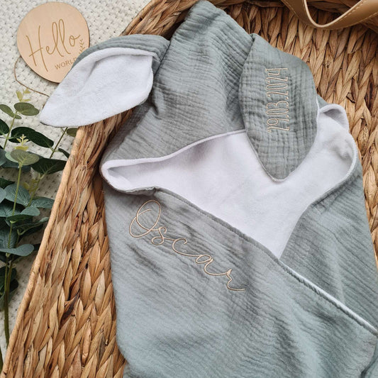 Personalised hooded baby towel with embroidered name 'Oscar' and bunny ears. Made from soft organic cotton muslin and terry, perfect for newborns.