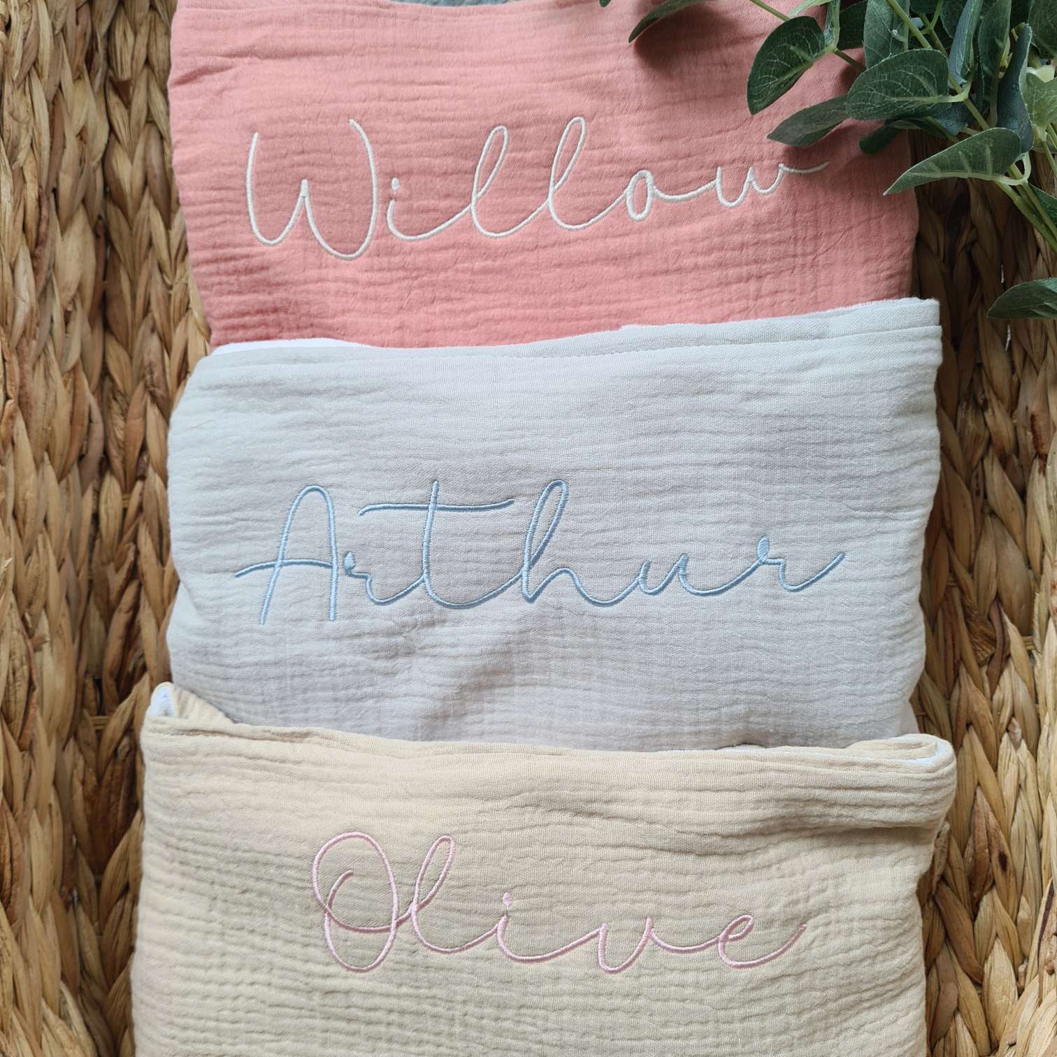 Stacked personalised baby towels in pink, grey, and beige, with embroidered names 'Willow', 'Arthur', and 'Olive'. Soft and gift-ready.